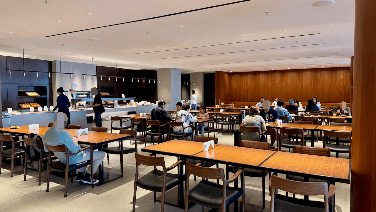 寬敞的餐廳內賓客於木製餐桌用餐,背景設有自助餐檯及廚師備餐區。