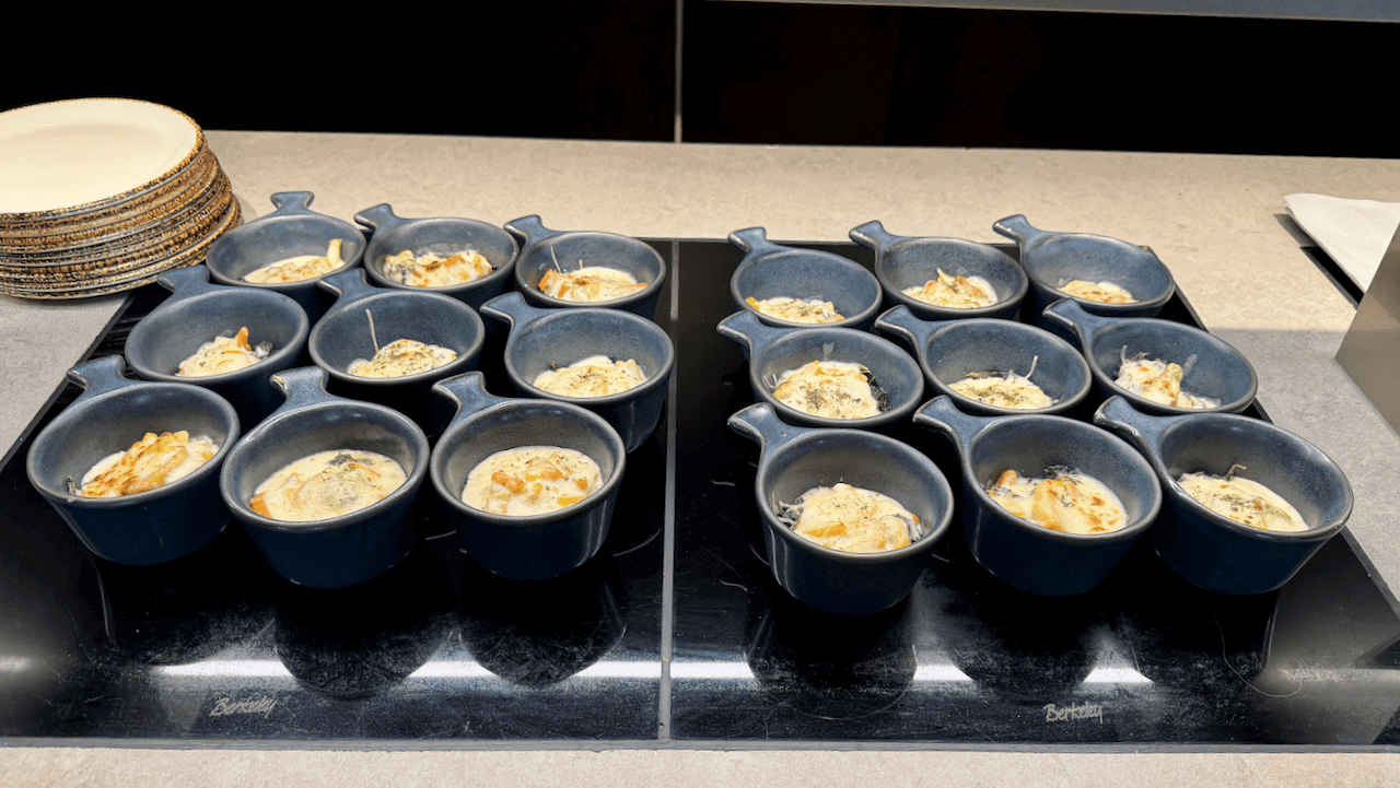 多個深藍色陶瓷小碗盛載焗烤奶油菜餚,排列於自助餐枱上
