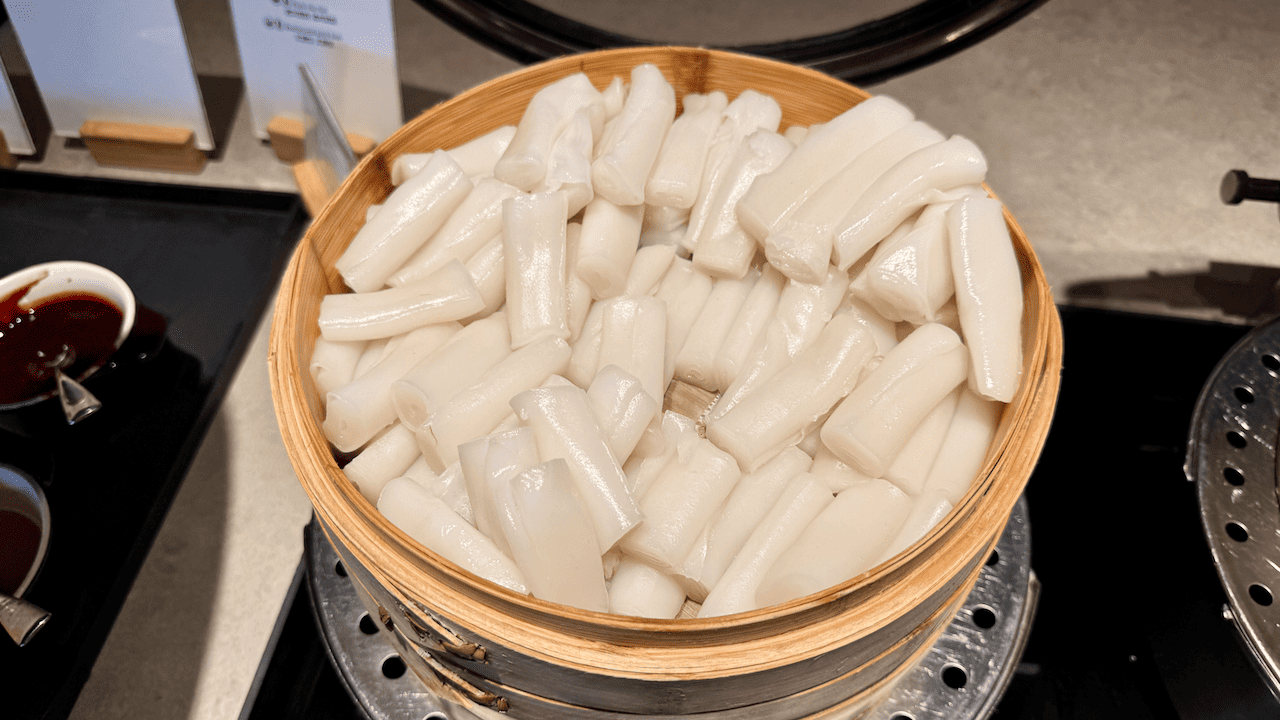 竹蒸籠內盛滿白色年糕條,旁邊備有醬油碟